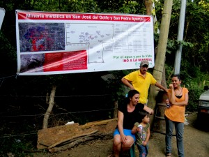 A family stands under a banner showing the proposed mining licenses in their communities. La Puya, Guatemala